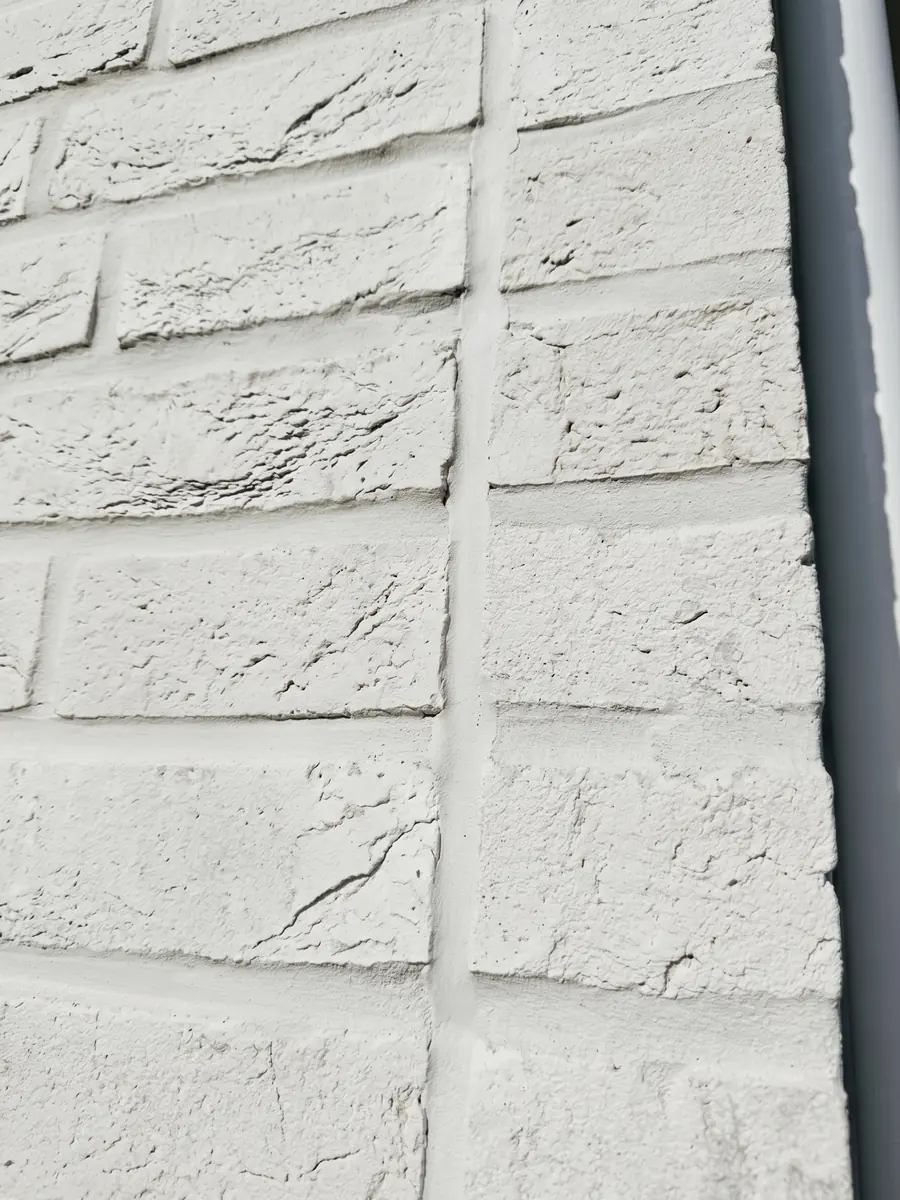Senkrechte elastische Dehnungsfuge in einer weiß gestrichenen Klinkerfassade neben einem Fallrohr
